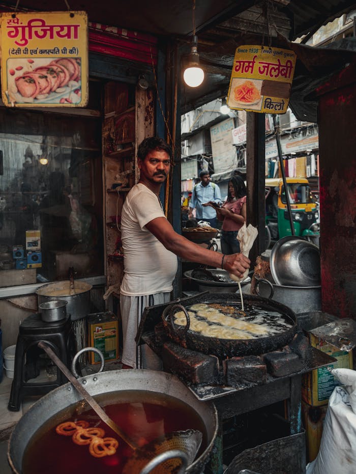 services-01 A street vendor prepares jalebi on a busy street in Delhi, showcasing Indian culinary tradition.