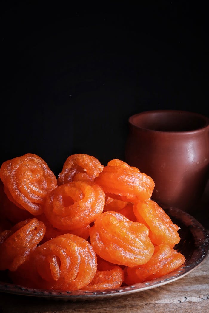 about-us Appetizing orange jalebi sweets on a plate with a moody dark background, showcasing vibrant Indian dessert.